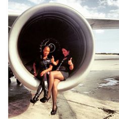 two people sitting on the back of an airplane engine with thumbs up and one person wearing black boots