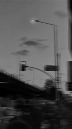 black and white photograph of traffic at an intersection with street lights in the background on a cloudy day