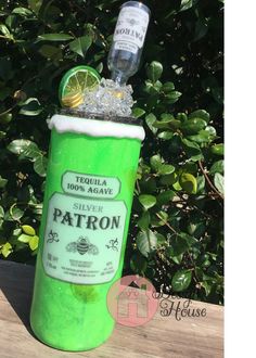 there is a green bottle with ice and lemon in it on the table next to some bushes