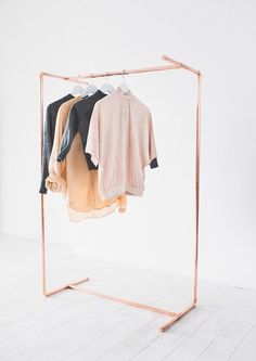 clothes are hanging on the rack in front of a white wall and wooden flooring