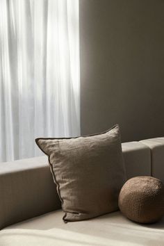 a couch with two pillows and a round pillow on top of it in front of a window