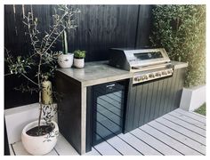 an outdoor kitchen with a grill and potted plants on the counter top next to it