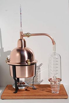 a copper colored coffee pot on a wooden tray next to a shot glass and a decanter