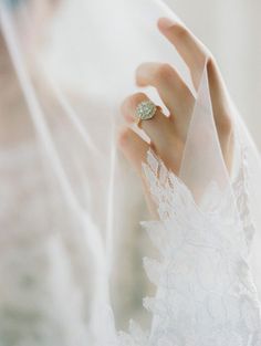 a close up of a person wearing a wedding ring on their finger and veil over her face