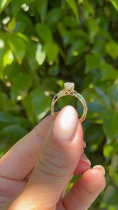 a person holding up a ring with a diamond on it in front of some leaves