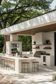 an outdoor kitchen with bar stools next to it and trees in the back ground