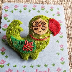 a green brooch with a red hat on it's head sitting on top of a piece of fabric