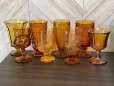 several different colored glasses sitting on top of a wooden table with white marble wall in the background