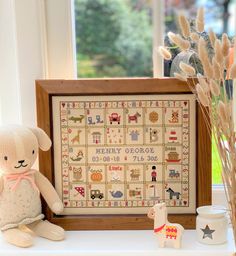 a stuffed animal sitting next to a framed cross stitch pattern