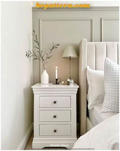 a white nightstand with two candles on it next to a bed