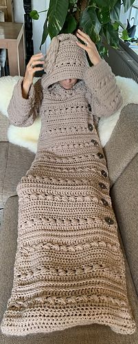 a woman sitting on top of a couch covered in a crocheted blanket and covering her face