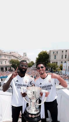 two men standing next to each other in front of a crowd holding up a trophy