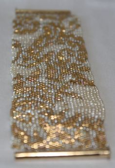 a gold and white beaded bracelet on a white tablecloth with beads in the middle