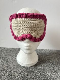 a white mannequin head wearing a crocheted pink and white blindfold