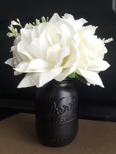 a black mason jar with white flowers in it