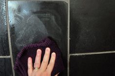 a person's hand on top of a purple mitt next to a black tiled wall