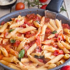 a skillet filled with pasta and sauce on top of a table next to tomatoes