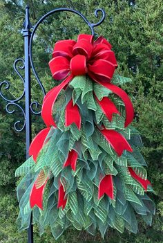 a red and green christmas tree hanging from a metal pole in front of some trees