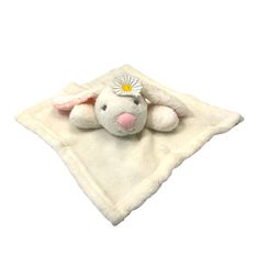 a small stuffed animal laying on top of a white blanket with a daisy in it's ear