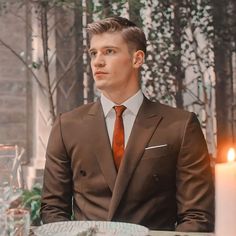 a man wearing a suit and tie sitting at a table with candles in front of him