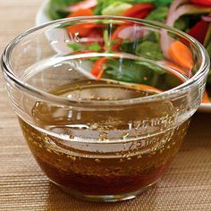 a salad with dressing in a glass bowl next to a plate full of salad greens