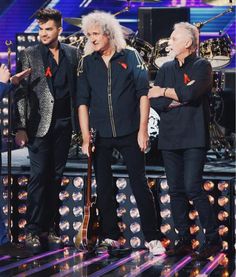 three men standing on stage next to each other and one is holding a guitar in his hand