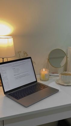 a laptop computer sitting on top of a white desk next to a candle and mirror