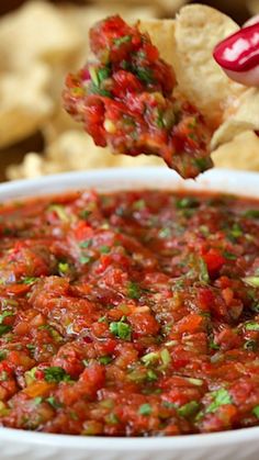 a person dipping salsa into a white bowl with tortilla chips in the background