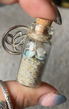 a person is holding a tiny bottle filled with sand and shells