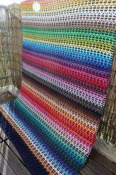 a multicolored crocheted blanket sitting on top of a wooden floor next to a fence