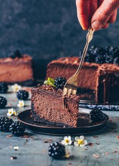 a piece of chocolate cake on a plate with a fork in it and some blackberries