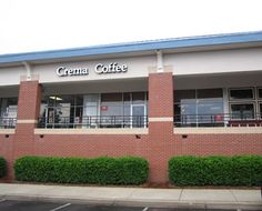 the front of a coffee shop with bushes and shrubs on the side of the building