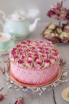 there is a pink cake on the table with teapots and cups in the background