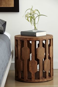 a wooden side table with a book and plant on it next to a white bed