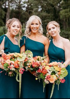 three bridesmaids in green dresses holding their bouquets and smiling at the camera