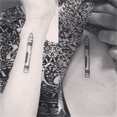 two people with matching tattoos on their arms holding up pencils and writing utensils