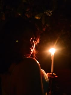 a woman holding a lit candle in the dark