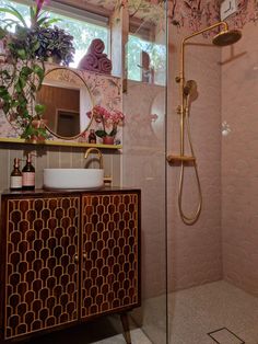 a bathroom with pink tile and gold fixtures, including a shower head, sink, mirror, and cabinet