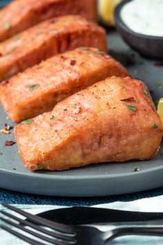 two pieces of fish on a plate with lemon wedges next to some sauce and a fork