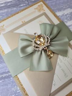 a close up of a wedding card with a bow and brooch on it's side