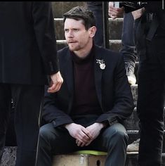 a man sitting on top of a stool next to some stairs with other people standing behind him