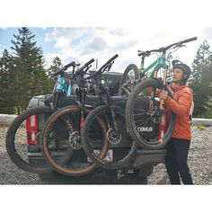 a man standing next to a truck with bikes on it's back and holding onto the bike rack