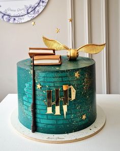 a green cake with gold decorations and books on top is sitting on a white table