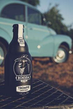 a bottle of beer sitting on top of a table next to an old blue car