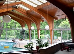 an indoor swimming pool with wooden ceiling and large windows on the sides, surrounded by potted plants