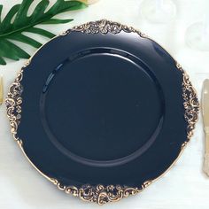 a black plate sitting on top of a table next to silverware and a green plant