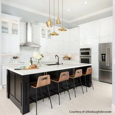 a kitchen with white cabinets and gold pendant lights hanging from the ceiling over the island