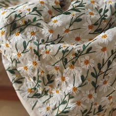 a white and yellow flowered fabric with green leaves on it's side, laying on a wooden surface