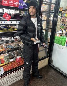 a man standing in front of a vending machine at a grocery store wearing a black jacket and hat