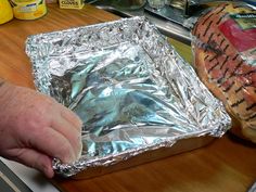 a person holding aluminum foil over a hot dog bun on top of a wooden table